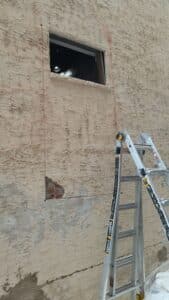 A plaster covered brick wall with a ladder and a hole about to be cut out. 