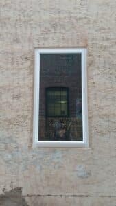 A large window that is located inside of a stucco and plaster covered brick wall. 
